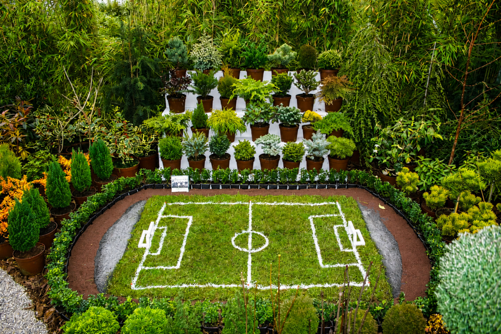 Miniatur-Fußballfeld aus Rasen, umgeben von vielen Topfpflanzen und Gehölzen auf einer Hausmesse.